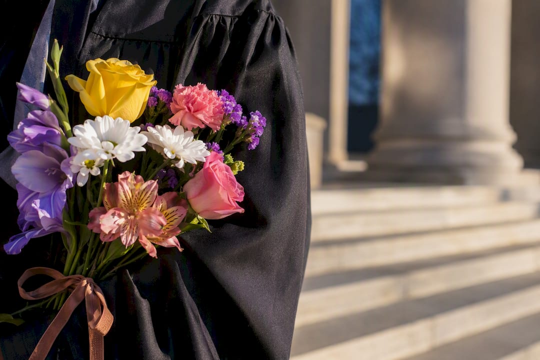 Cropped graduation flowers beside academic gown